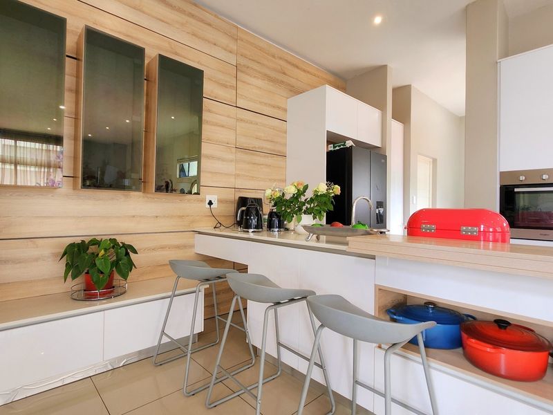 Modern kitchen featuring light wood-grain cabinetry, a functional island with breakfast bar seating, integrated oven, and sleek tiled flooring.