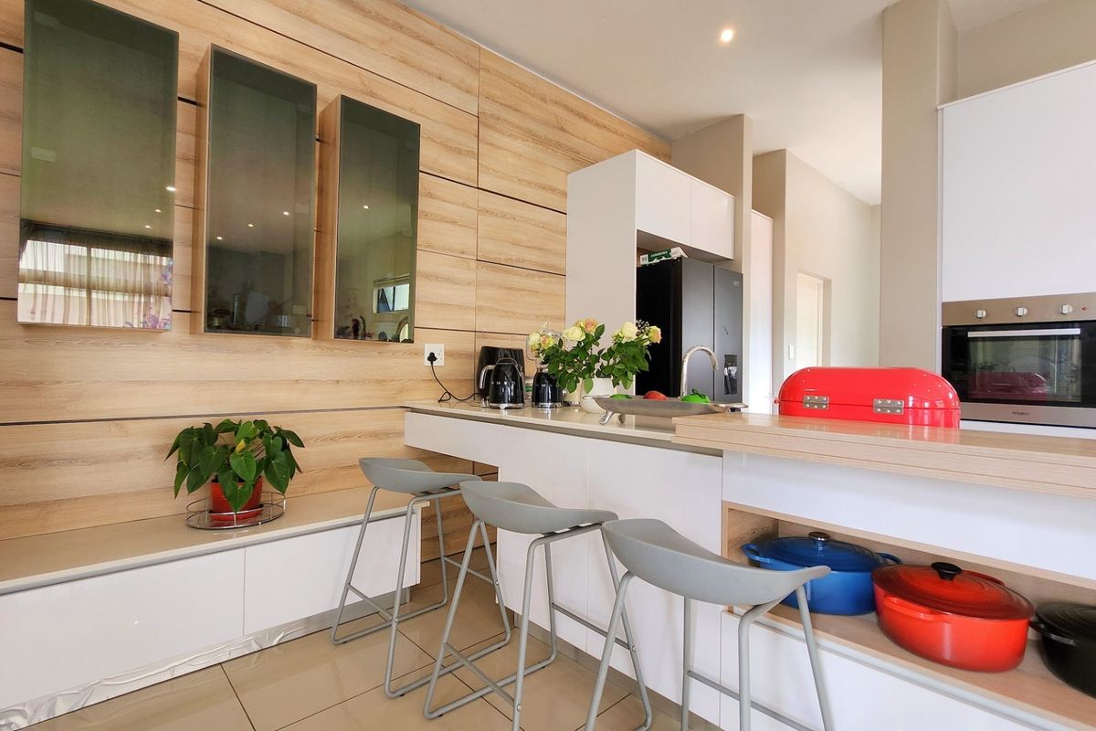 Modern kitchen featuring light wood-grain cabinetry, a functional island with breakfast bar seating, integrated oven, and sleek tiled flooring.