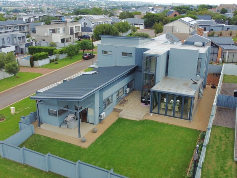 Aerial view of a modern multi-level residential property featuring a metal roof, paved patio areas, and a well-maintained garden within a secure estate.