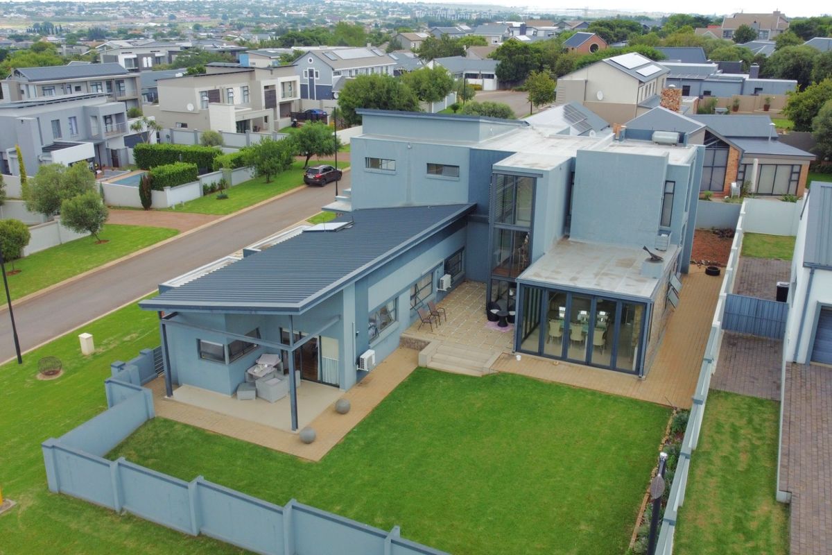 Aerial view of a modern multi-level residential property featuring a metal roof, paved patio areas, and a well-maintained garden within a secure estate.