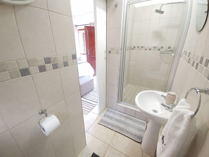 A compact bathroom featuring a pedestal basin, a glass-enclosed shower, and neutral ceramic tiling throughout.