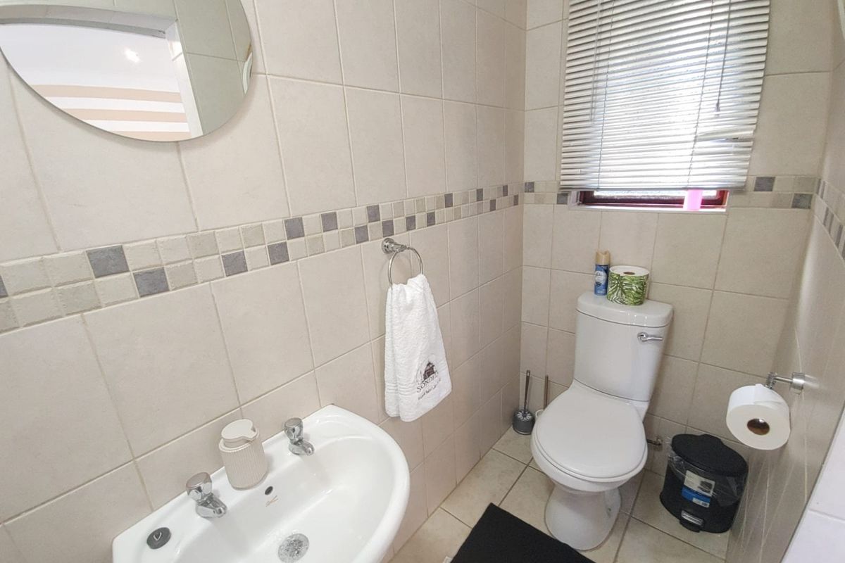 A functional bathroom featuring neutral ceramic wall and floor tiles, a pedestal basin, and a dual flush toilet with window blinds.
