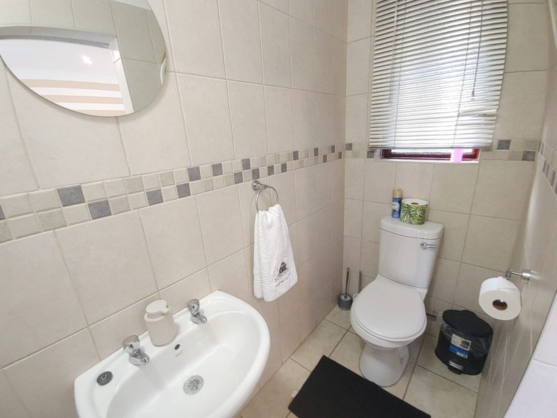 A functional bathroom featuring neutral ceramic wall and floor tiles, a pedestal basin, and a dual flush toilet with window blinds.