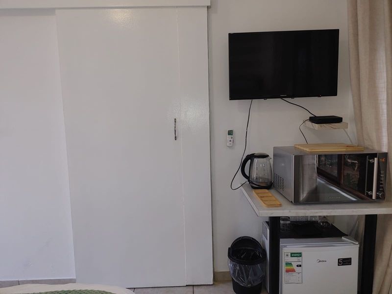A bedroom area featuring a sliding door, wall-mounted television, and a compact kitchenette station with a microwave and mini-fridge.