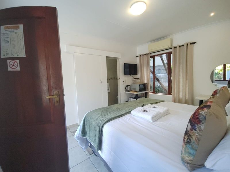 A functional bedroom featuring tiled flooring, an integrated air conditioning unit, and a sliding door leading to an en-suite bathroom.