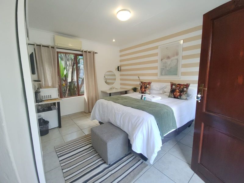 A well-lit bedroom featuring tiled flooring, an integrated air conditioning unit, and a built-in desk area with direct access to natural light.