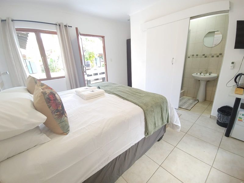 A bedroom featuring tiled flooring, direct outdoor access, and an en-suite bathroom with a pedestal basin and shower.