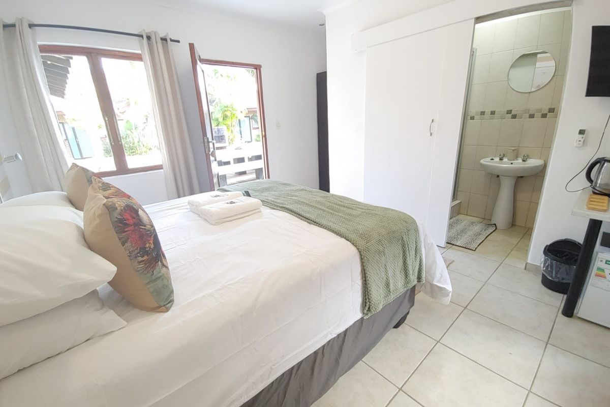 A bedroom featuring tiled flooring, direct outdoor access, and an en-suite bathroom with a pedestal basin and shower.