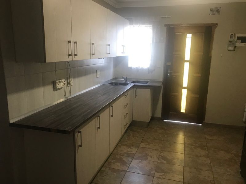 A functional kitchen featuring laminate countertops, built-in cabinetry, and tiled flooring, offering a practical layout with direct access to an exterior door.