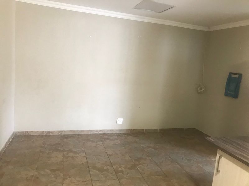An empty open-plan living area featuring tiled flooring, neutral walls, and partial view of kitchen cabinetry.
