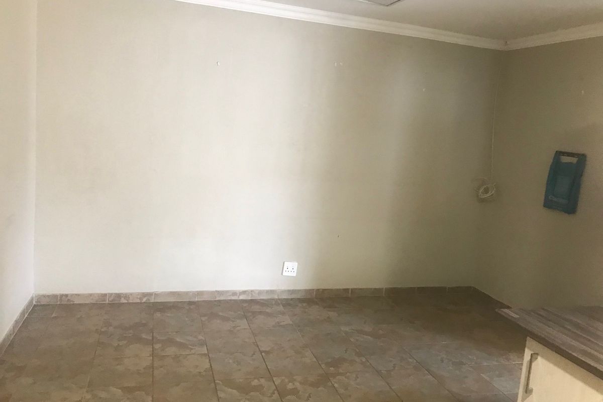 An empty open-plan living area featuring tiled flooring, neutral walls, and partial view of kitchen cabinetry.