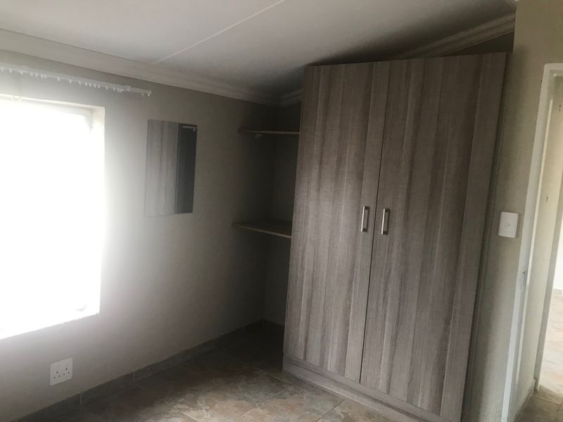A bedroom featuring tiled flooring, coving, and a built-in wardrobe with open shelving.