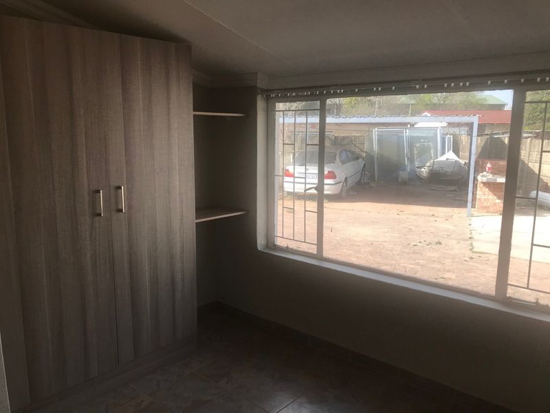 A bedroom featuring built-in wardrobes, open shelving, tiled flooring, and a large window with security bars overlooking the rear yard.