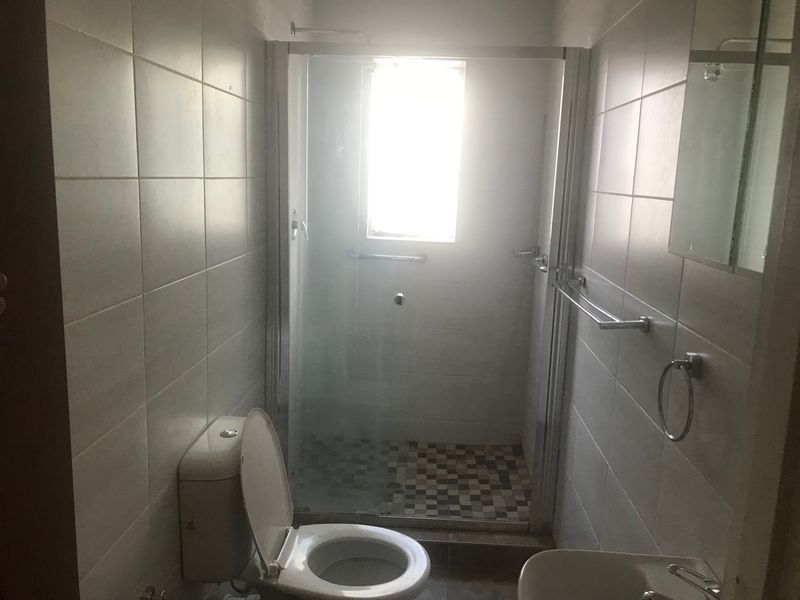 A functional bathroom featuring a glass-enclosed shower, tiled walls, and standard sanitary fixtures, offering a clean and practical layout.