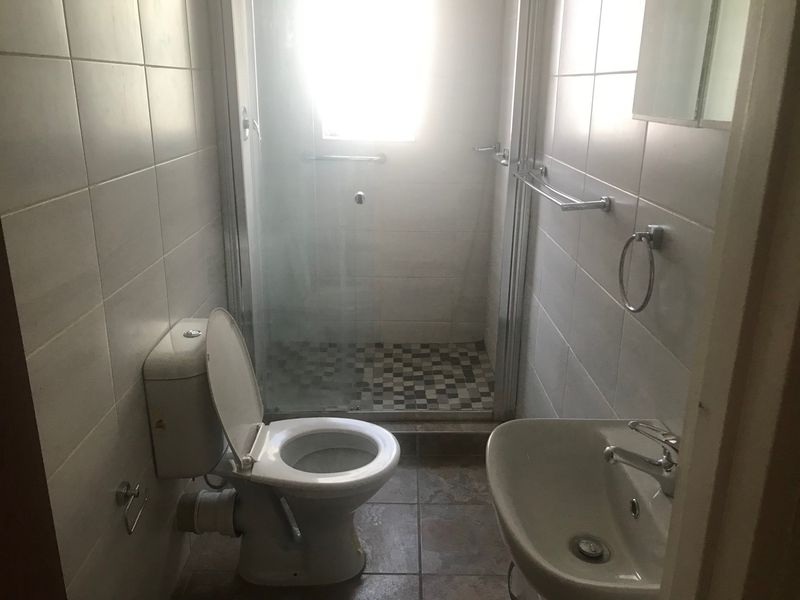 A functional bathroom featuring a shower enclosure, toilet, and washbasin with neutral wall and floor tiling.