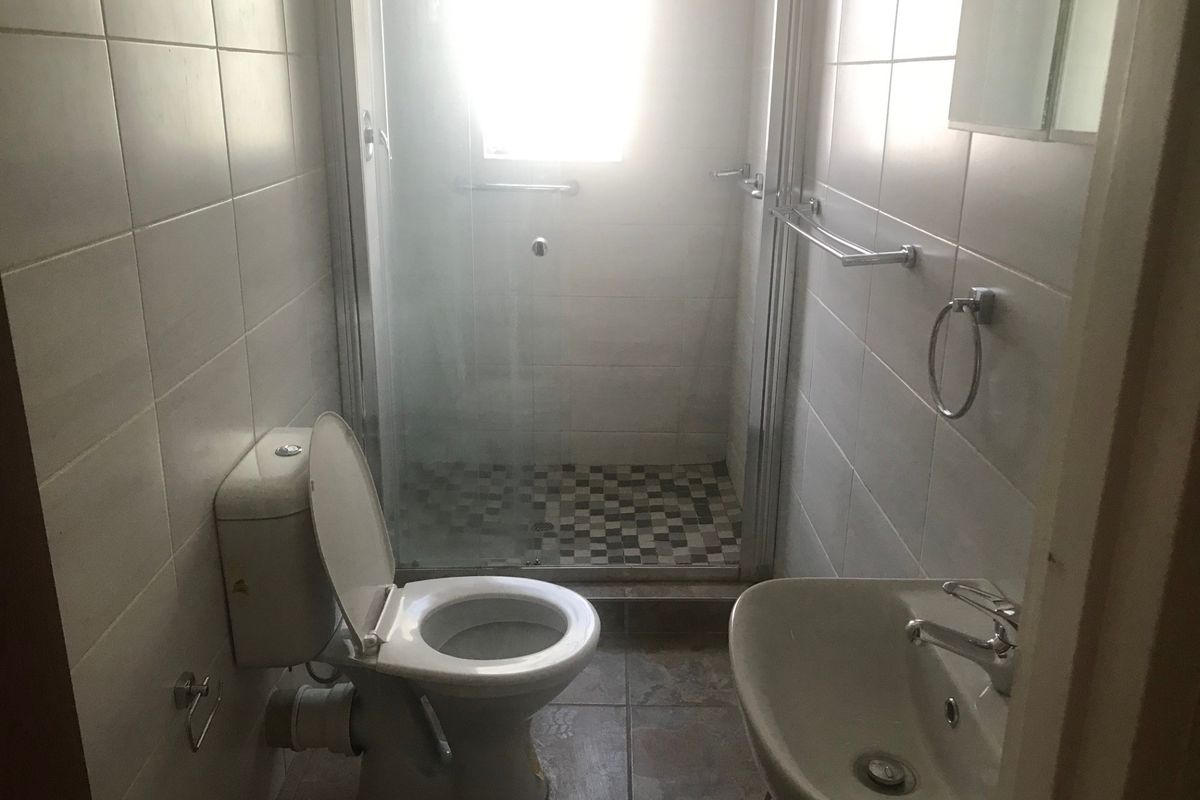 A functional bathroom featuring a shower enclosure, toilet, and washbasin with neutral wall and floor tiling.