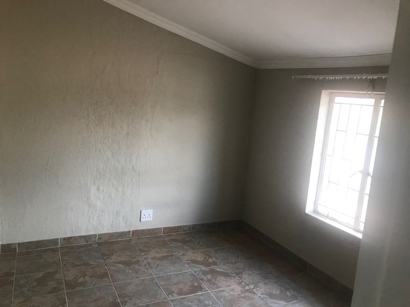 An empty bedroom featuring tiled flooring, a window with security bars, and neutral wall finishes.