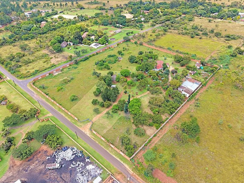 An aerial view of a large residential vacant land plot featuring established trees, perimeter walling, and existing outbuildings in a semi-rural setting.
