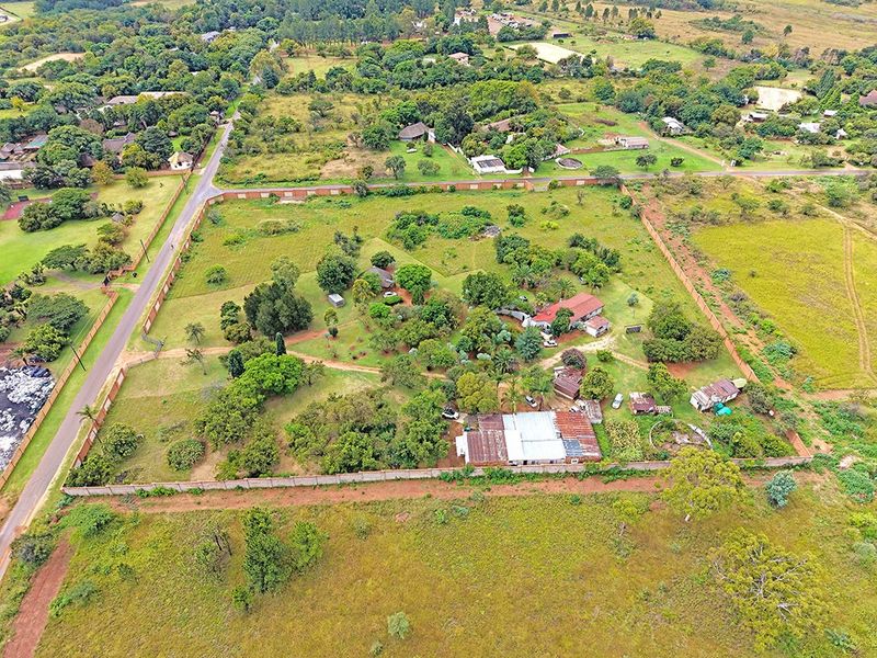 Aerial view of a large residential plot featuring mature trees, established perimeter walls, and existing outbuildings on the property.