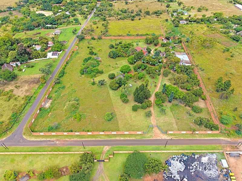 Aerial view of a large residential vacant land plot featuring mature trees, a perimeter brick wall, and gated access from the main road.