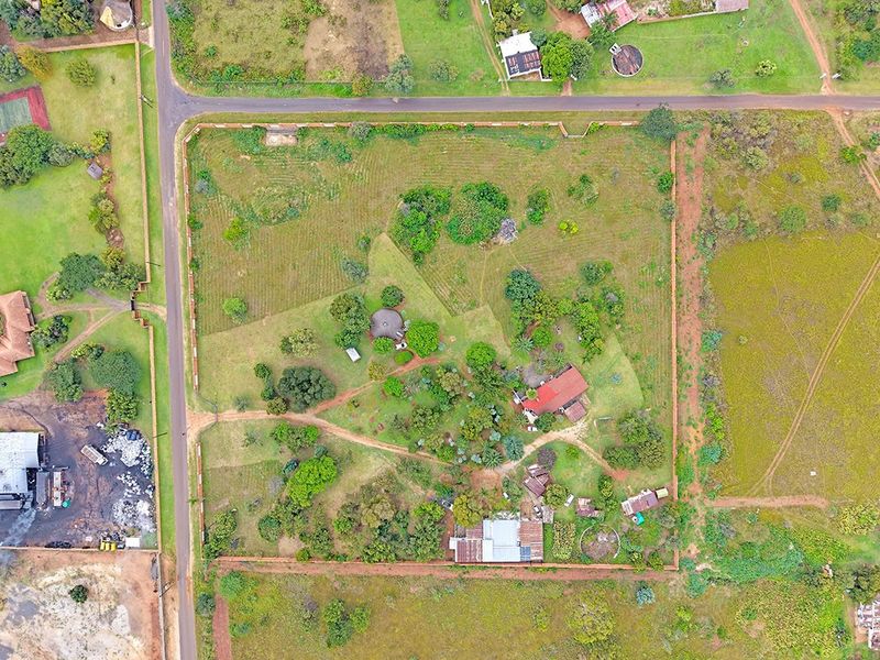 Aerial view of a large residential vacant land plot featuring established trees, perimeter fencing, and existing structures on the property.