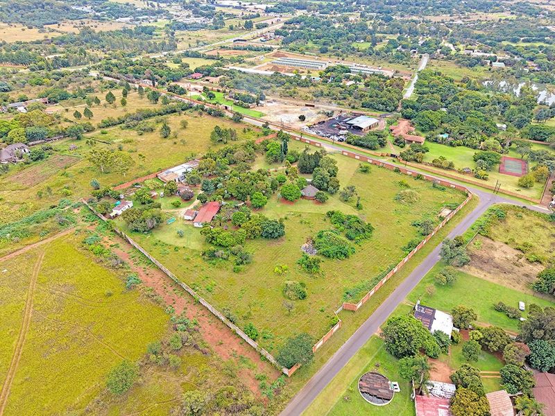 Aerial view of a large residential plot featuring established trees, perimeter walling, and existing structures within a semi-rural neighborhood setting.