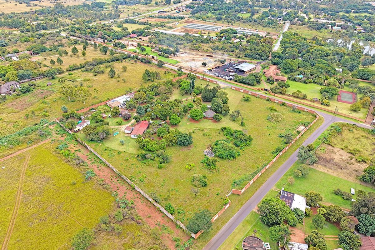 Aerial view of a large residential plot featuring established trees, perimeter walling, and existing structures within a semi-rural neighborhood setting.
