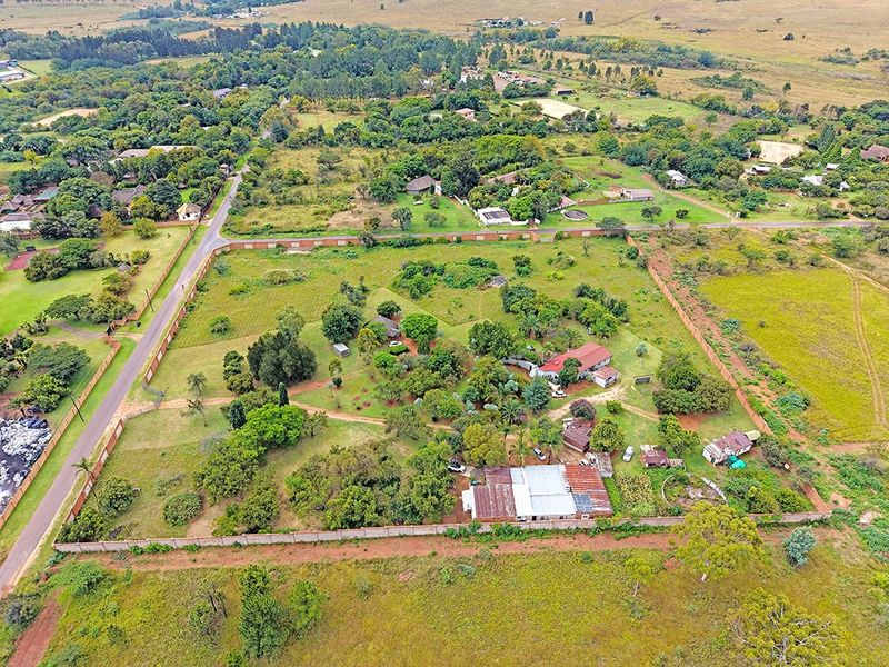 Aerial view of a large residential plot featuring established trees, perimeter walling, and multiple existing structures within a semi-rural neighborhood setting.