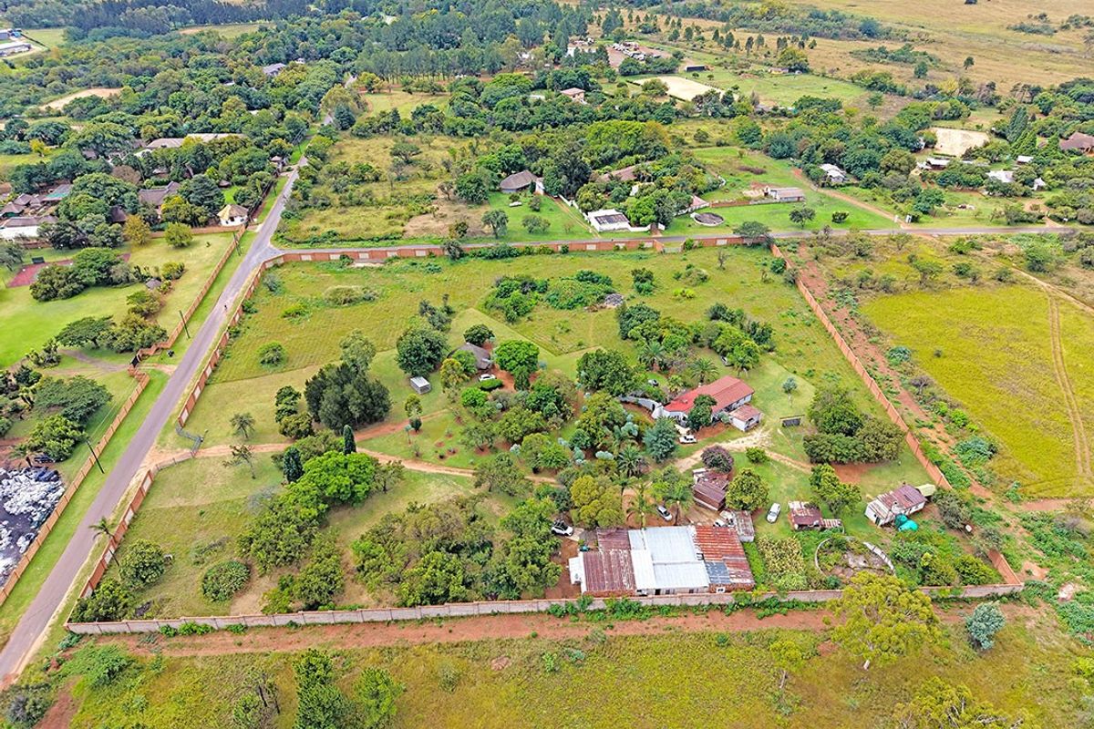Aerial view of a large residential plot featuring established trees, perimeter walling, and multiple existing structures within a semi-rural neighborhood setting.