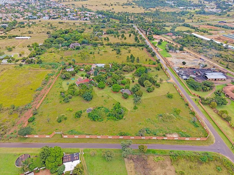 Aerial view of a large residential plot featuring established trees, perimeter walling, and existing structures within a suburban landscape.