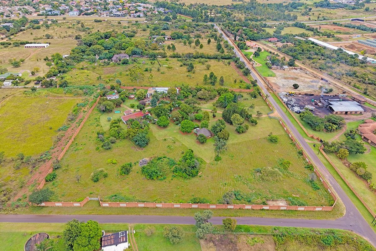 Aerial view of a large residential plot featuring established trees, perimeter walling, and existing structures within a suburban landscape.