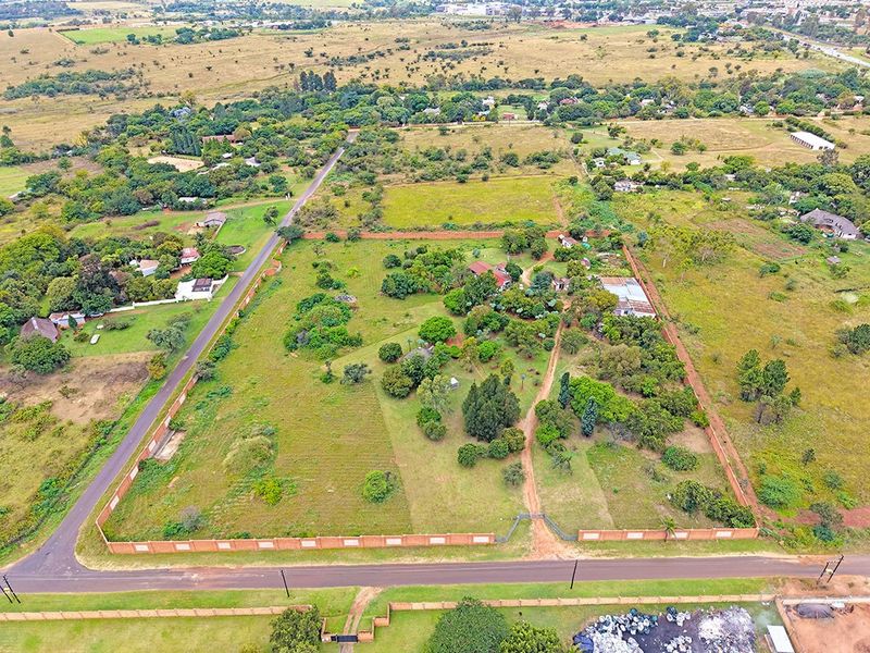 Aerial view of a large residential vacant land plot featuring a perimeter brick wall, mature trees, and existing structures with road access.