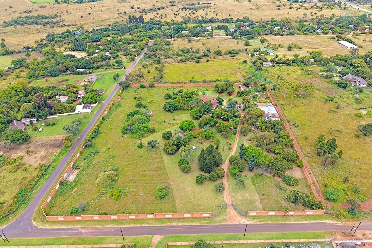 Aerial view of a large residential vacant land plot featuring a perimeter brick wall, mature trees, and existing structures with road access.
