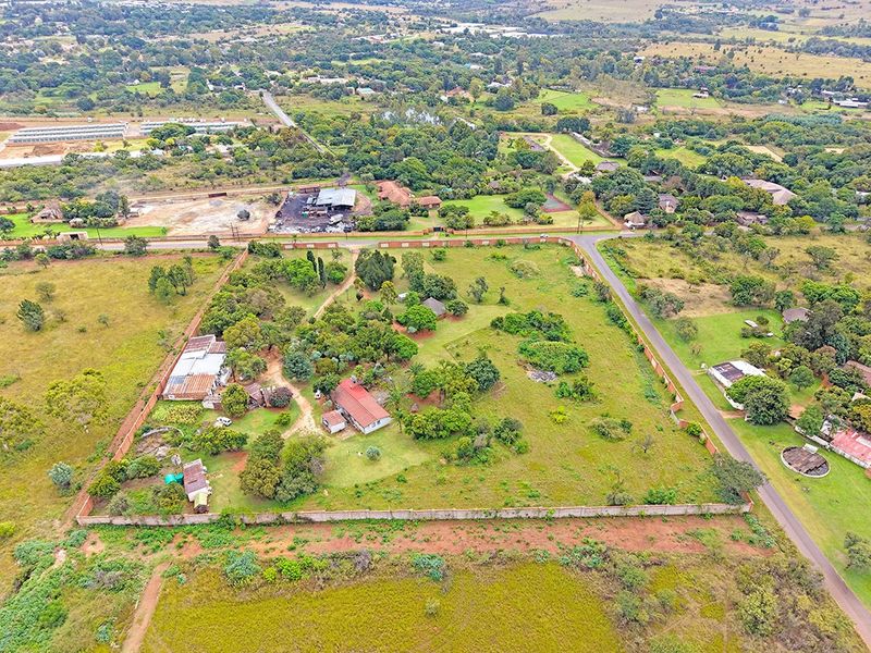 Aerial view of a large residential plot featuring established trees, multiple structures, and a perimeter wall, situated in a semi-rural neighborhood.