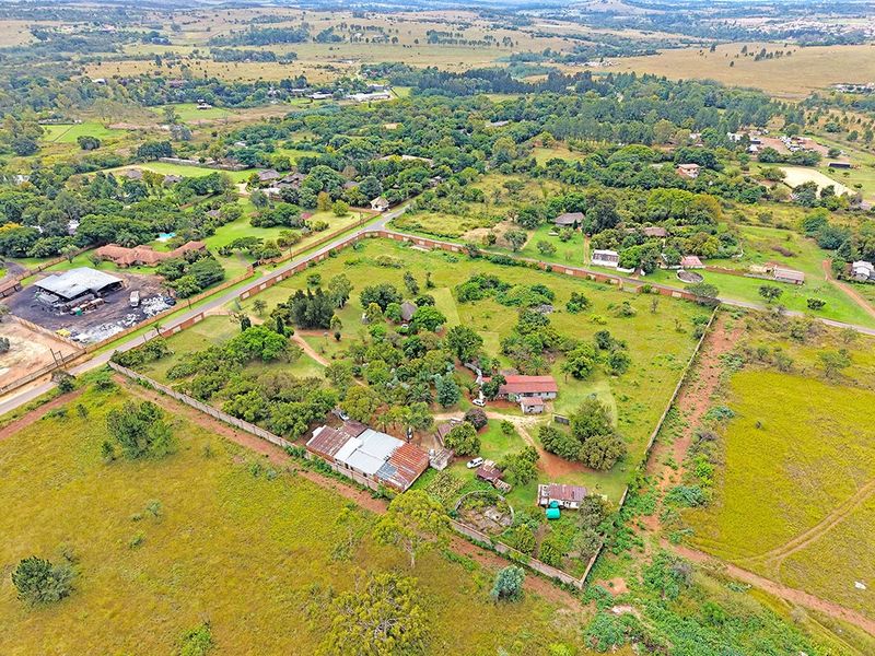 Aerial view of a large residential plot featuring multiple outbuildings, perimeter walling, and established trees within a rural landscape setting.