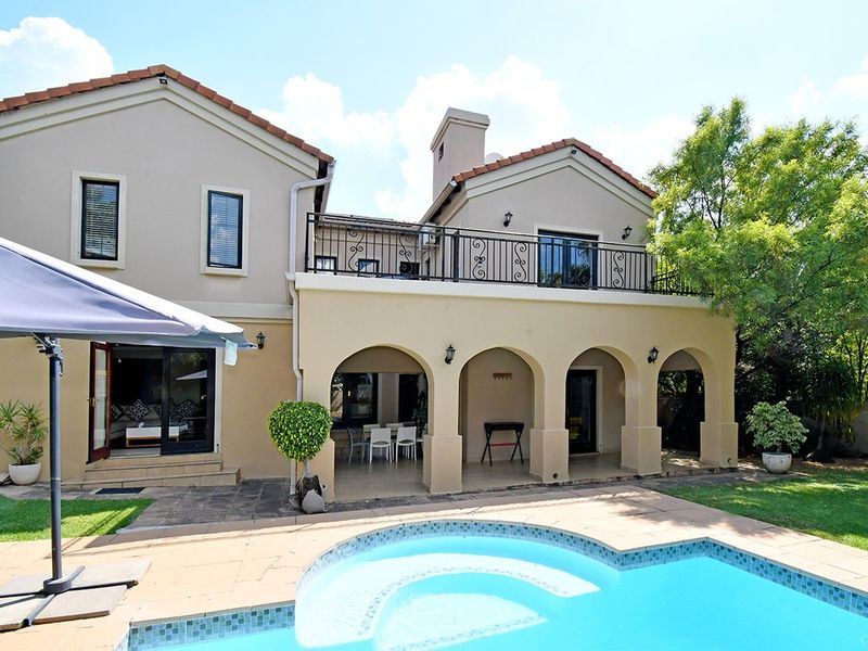 Rear view of the property featuring a swimming pool, covered patio with arched columns, and an upper-level balcony with wrought iron railings.