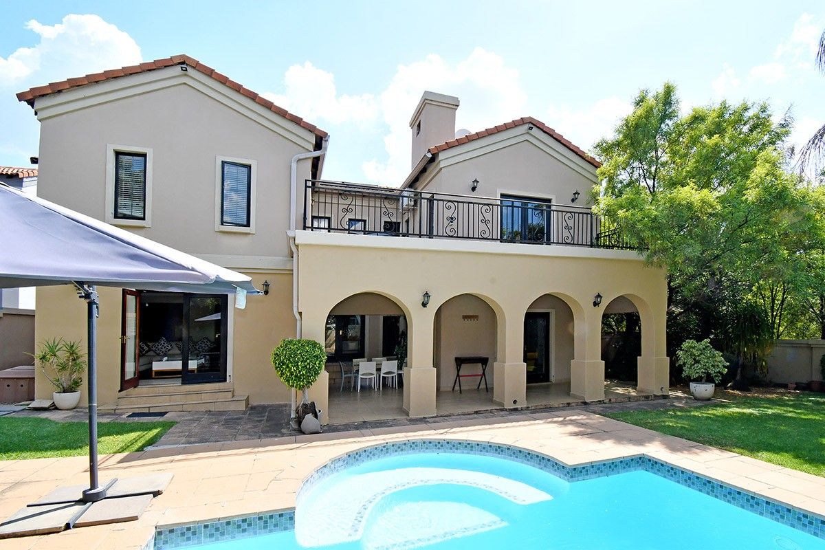 Rear view of the property featuring a swimming pool, covered patio with arched columns, and an upper-level balcony with wrought iron railings.