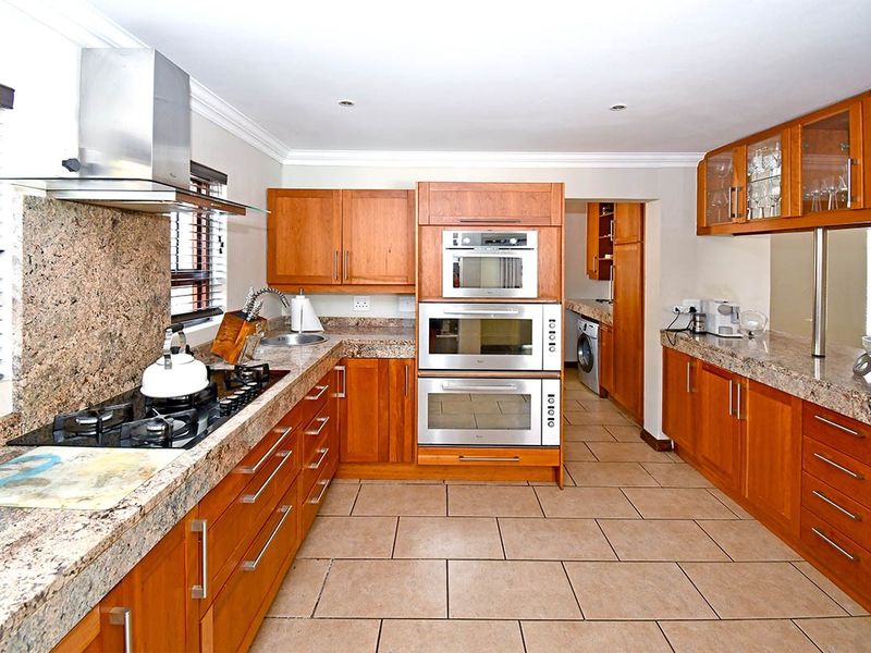 Spacious kitchen featuring warm wooden cabinetry, granite countertops, built-in stainless steel appliances, and a gas hob, with an adjoining scullery area.
