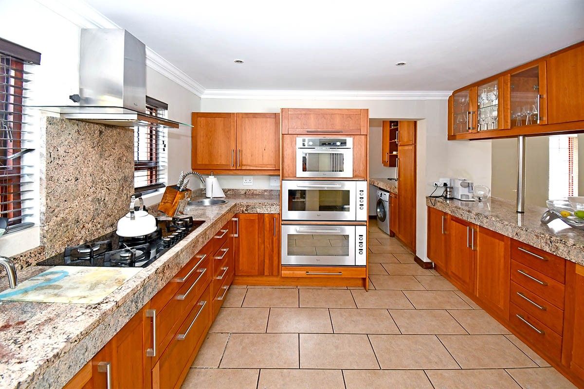 Spacious kitchen featuring warm wooden cabinetry, granite countertops, built-in stainless steel appliances, and a gas hob, with an adjoining scullery area.