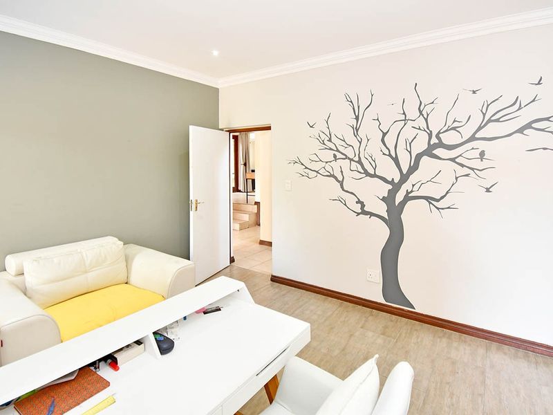 A well-lit bedroom featuring laminate flooring, coving, and recessed downlights, with a neutral color palette and a decorative wall decal.