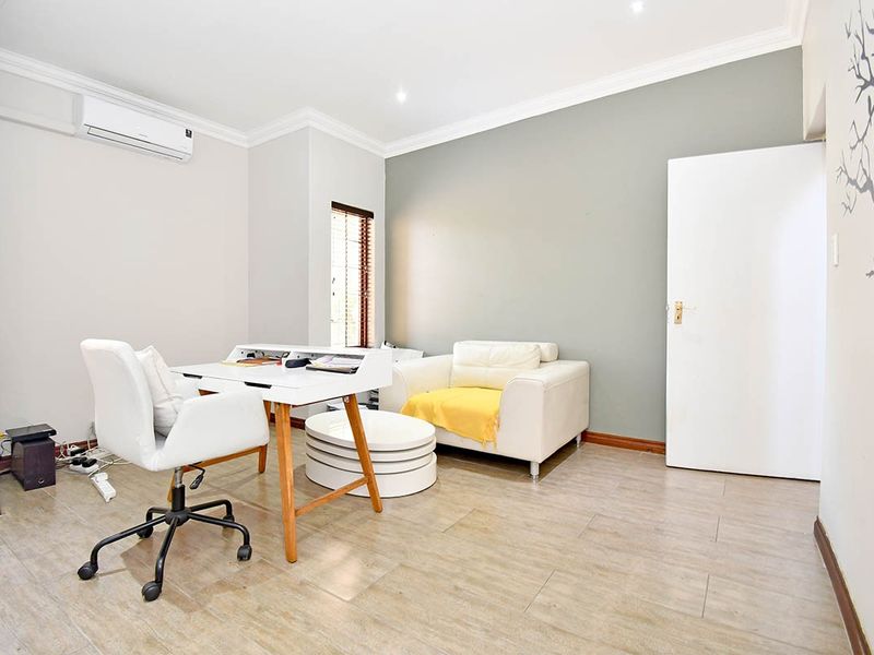 A bright and functional home office featuring timber-look tile flooring, modern cornicing, and a wall-mounted split-system air conditioner.
