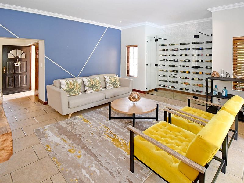 A bright living room featuring tiled floors, a striking blue accent wall, and a modern glass-enclosed built-in wine cellar.