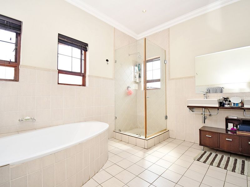 A spacious bathroom featuring a freestanding bathtub, a glass-enclosed shower, and dual wall-mounted washbasins with neutral tiled finishes throughout.