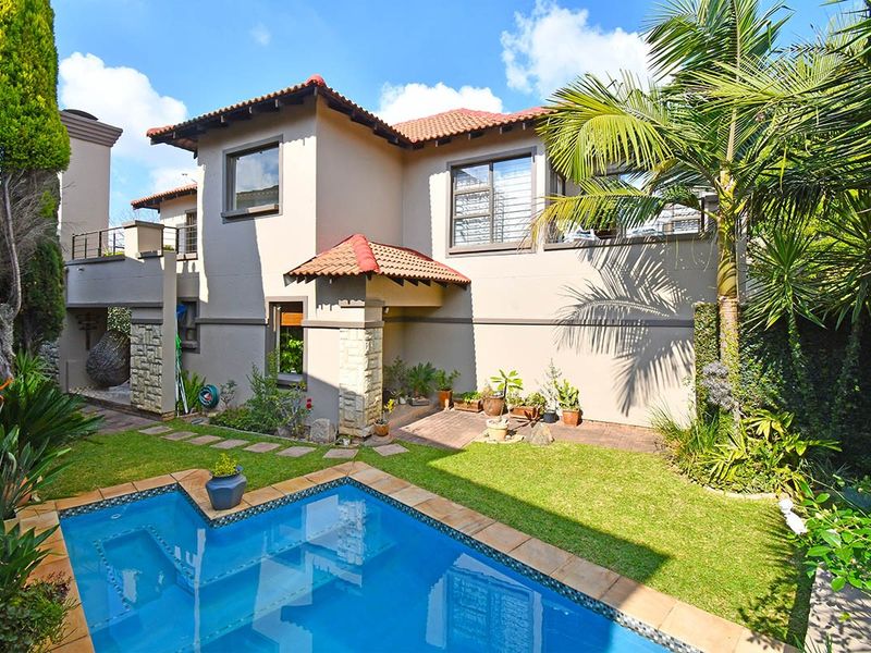 Rear view of the property featuring a well-maintained garden, a swimming pool, and a balcony overlooking the outdoor entertainment area.