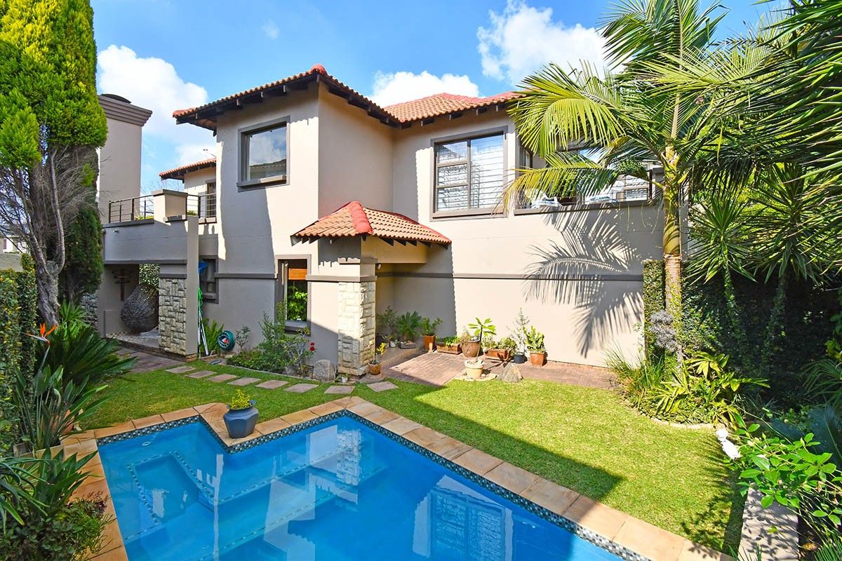 Rear view of the property featuring a well-maintained garden, a swimming pool, and a balcony overlooking the outdoor entertainment area.