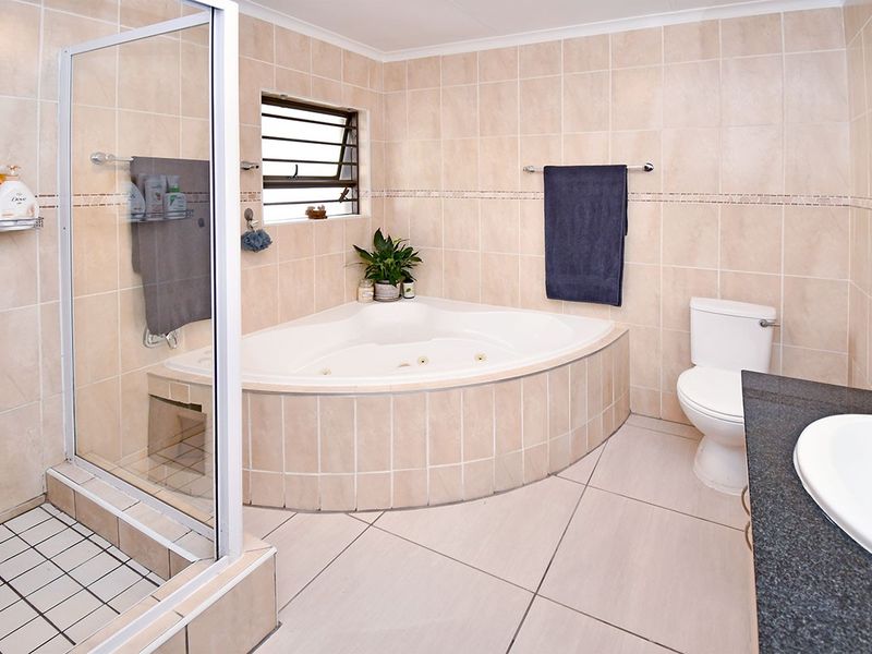 A well-maintained bathroom featuring a corner spa bath, a separate glass-enclosed shower, and a vanity with a dark countertop.