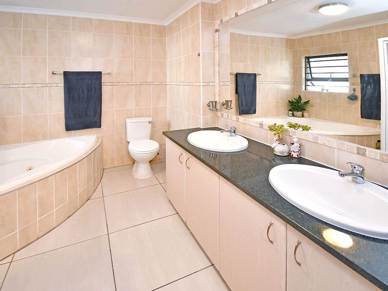 Spacious bathroom featuring a corner spa bath, dual vanity with granite countertop, and neutral ceramic tiling throughout.