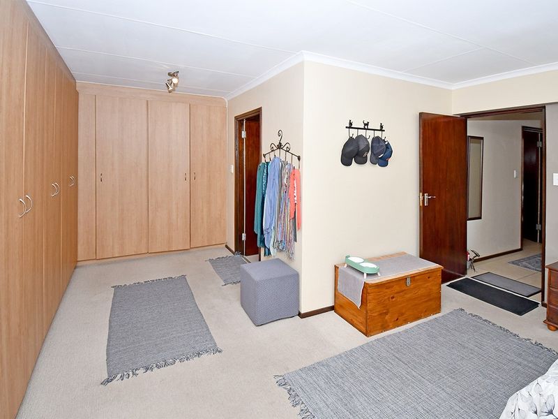 Spacious bedroom featuring extensive wall-to-wall built-in cupboards, neutral carpeting, and classic cove cornicing, offering ample storage and a functional layout.