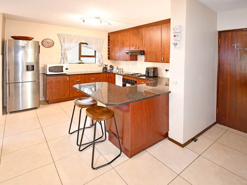A functional kitchen featuring wooden cabinetry, granite countertops, a breakfast bar, and built-in cooking appliances with tiled flooring throughout.