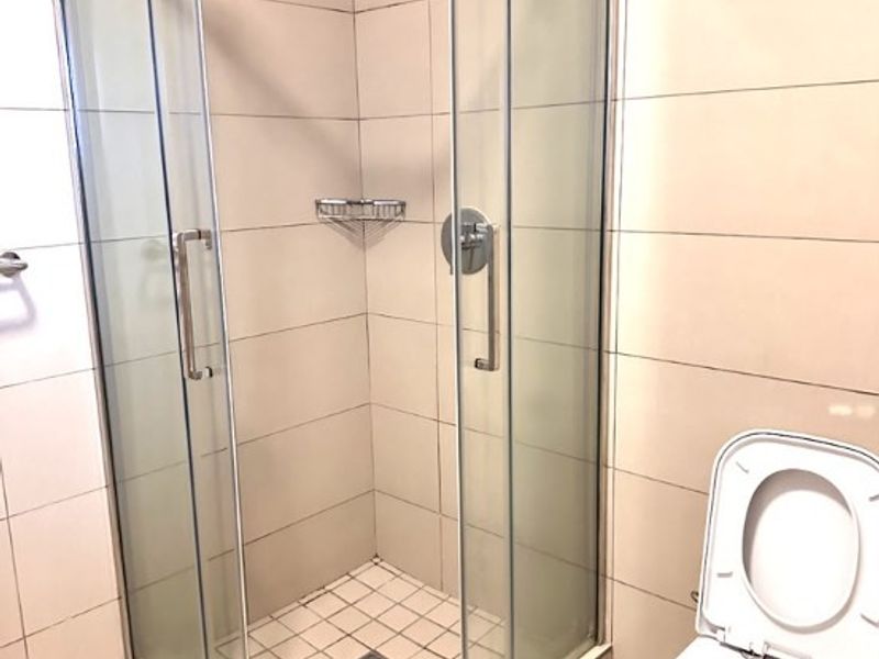 A clean, modern bathroom featuring a glass corner shower enclosure, tiled walls and flooring, and a standard toilet.
